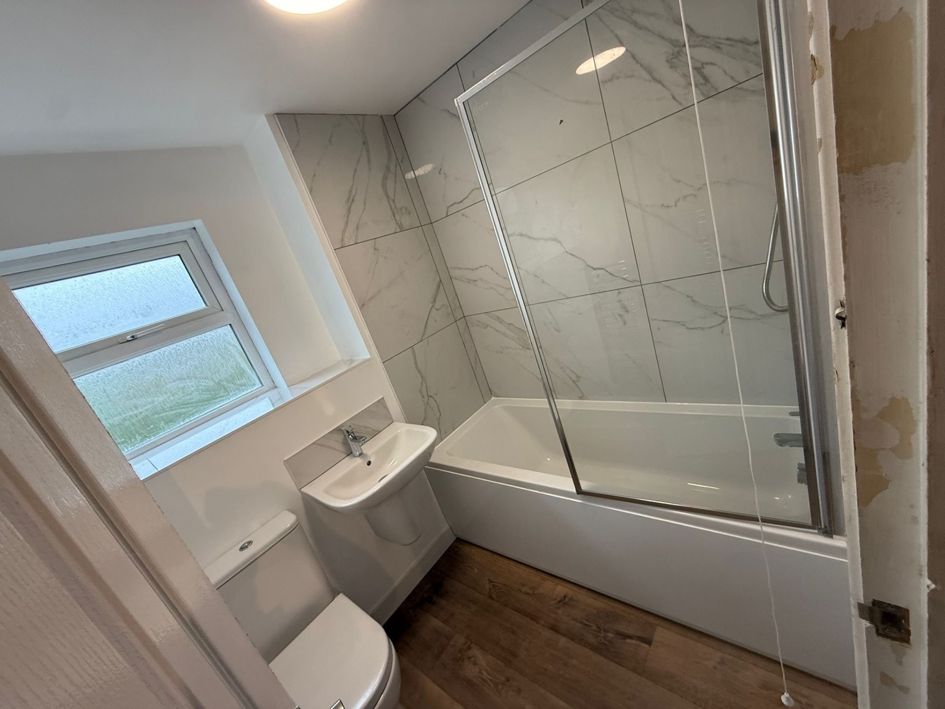 Grey tiled bathroom with panelled bath, screen and compact vanity
