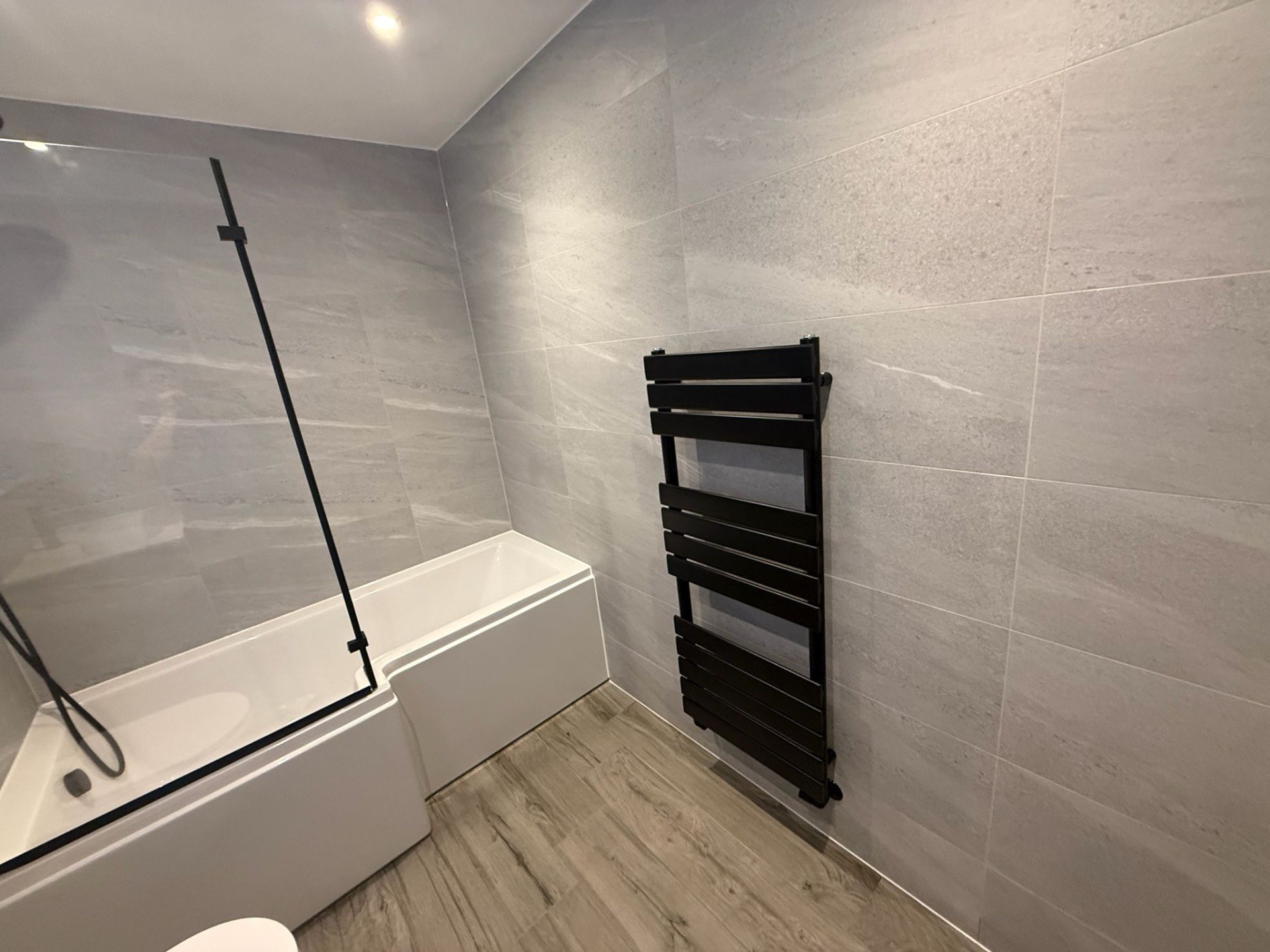 Newly fitted contemporary bathroom with stone-effect tiling and black heated towel rail