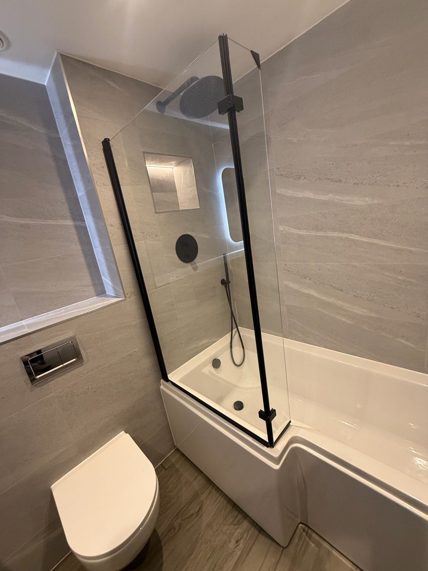 Stone-effect bathroom with shower over bath and black framed screen