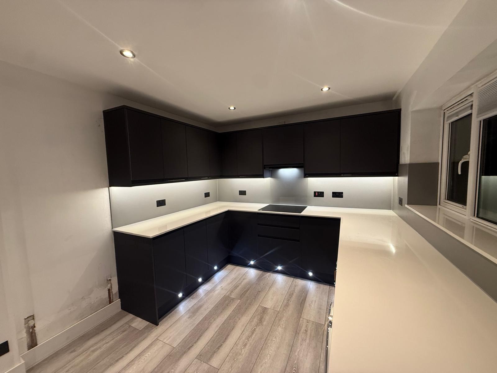 Dark fitted kitchen corner with seamless pale worktops and task lighting
