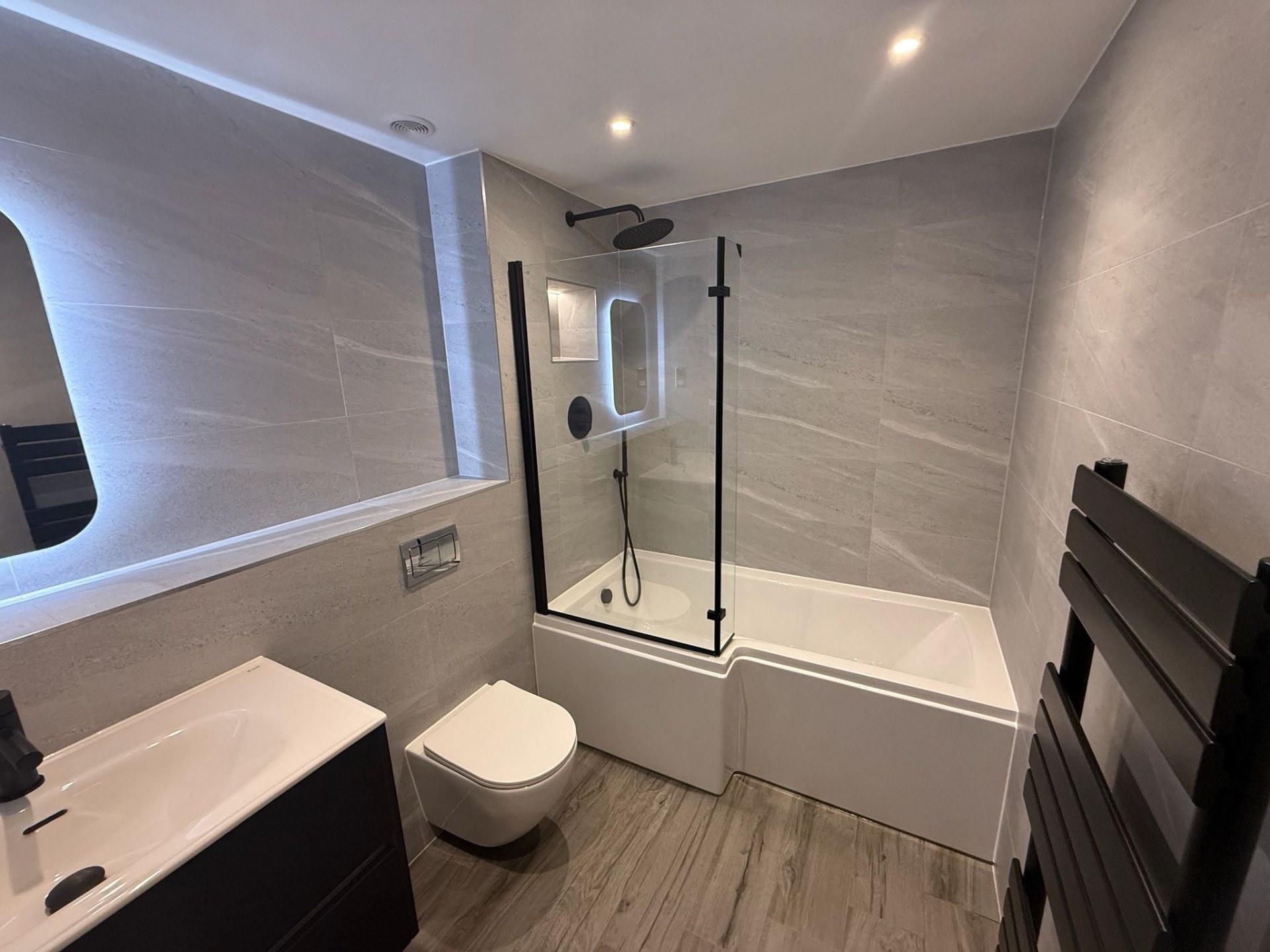Completed grey tiled bathroom with bath, screen and black fittings